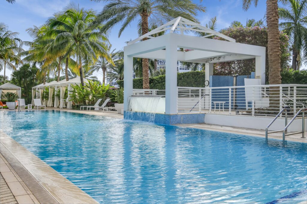 A pool with a gazebo and palm trees in the background.